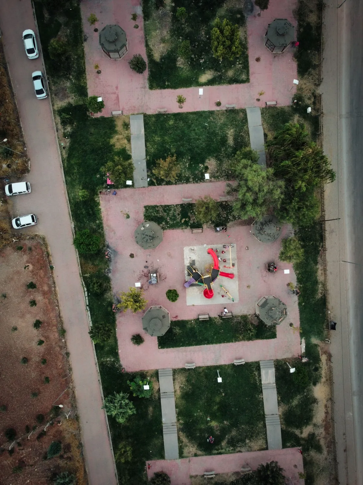 Widok z lotu ptaka na park z geometrycznymi alejkami, trawnikami i centralnym placem zabaw.