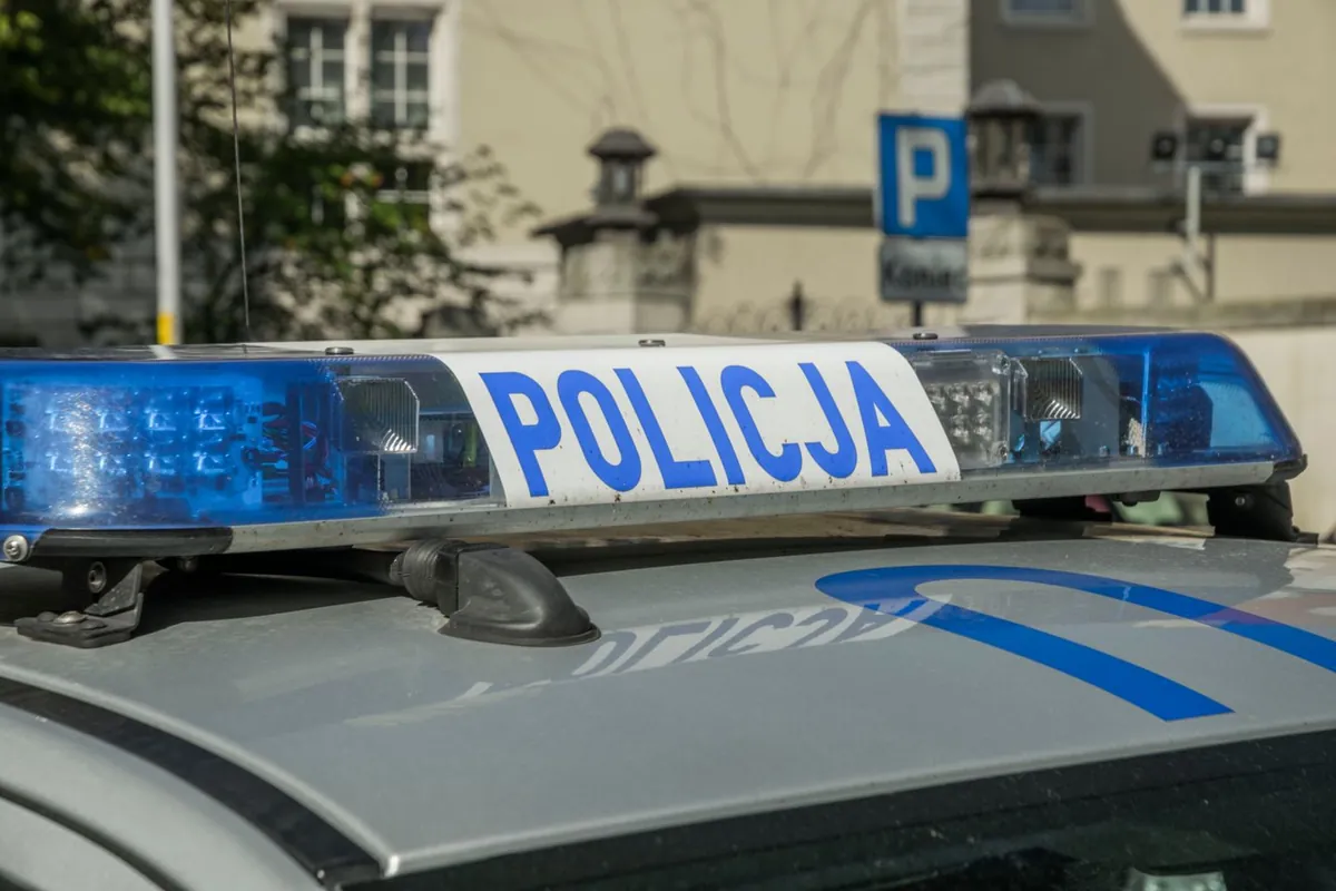 Na dachu radiowozu widać niebieskie światła i napis „POLICJA”.