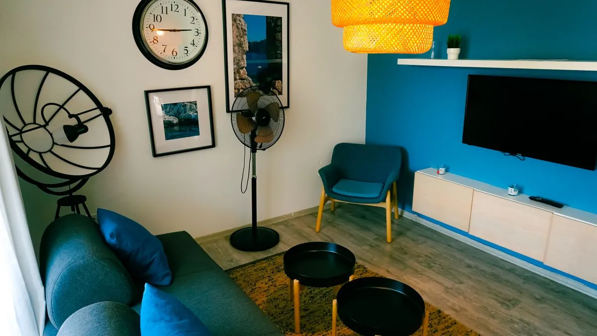 Salon z niebieskimi fotelami i ścianą, telewizorem, stolikiem oraz dekoracjami na ścianie.